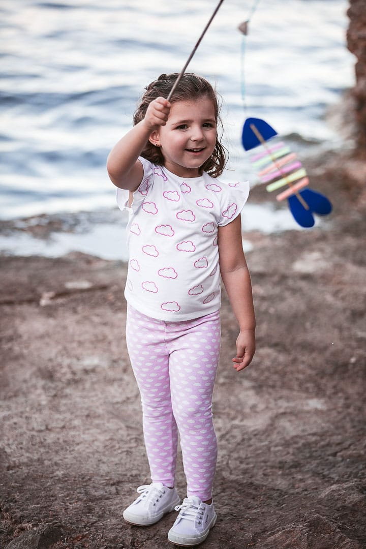 Photographic report of children's clothing with a girl dressed in skinny pants and a pink t-shirt playing on the jetty in Ibiza