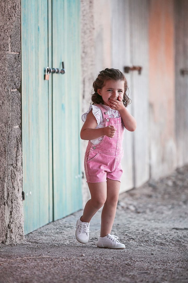 Photographic report of children's clothing with a girl dressed in pink overalls playing on the jetty in Ibiza