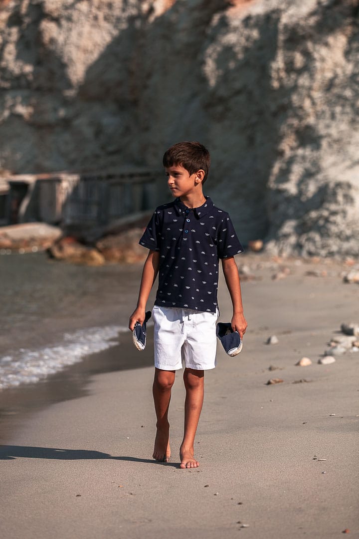 Photographic report of children's clothing with a child walking on the shore of Cala Dort beach in Ibiza