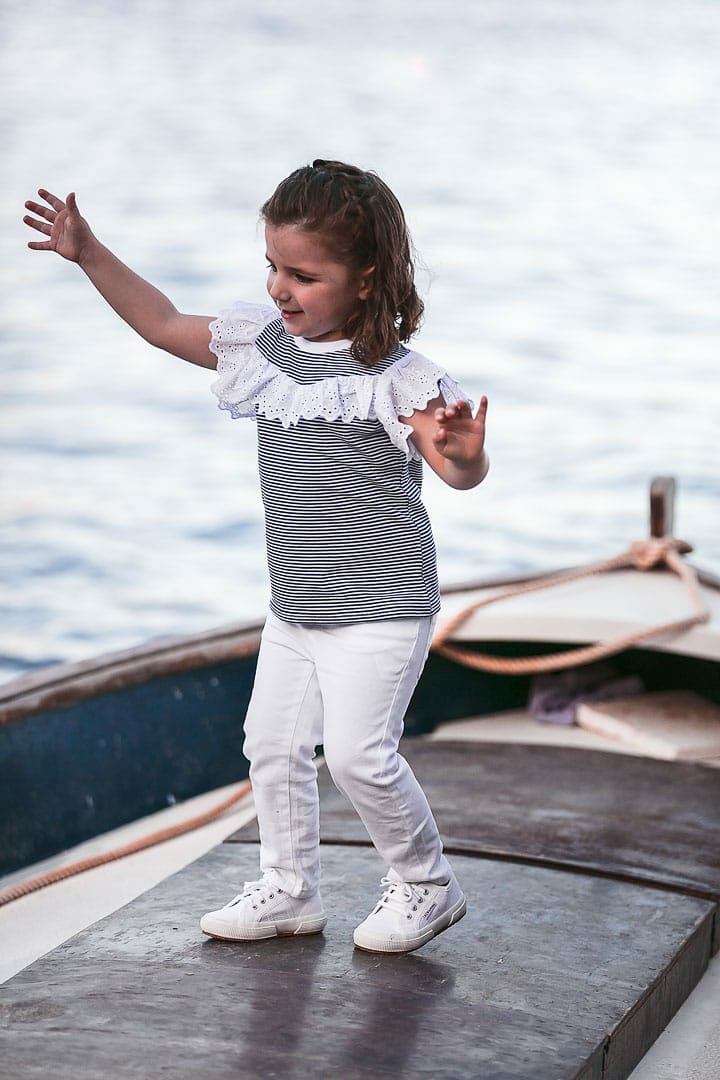 photograph of a smiling girl playing on a boat dressed in a blue striped t-shirt and white pants on a jetty in Ibiza